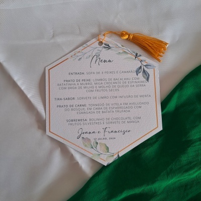 Cartão de menu hexagonal com texto em português sobre tecido branco e verde.