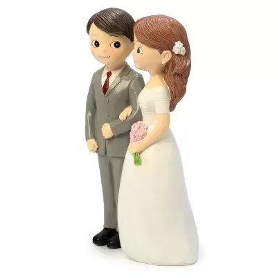 Figuras decorativas de noivo e noiva em resina, o noivo com fato cinzento e gravata vermelha, a noiva com vestido branco e ramo de flores cor-de-rosa.