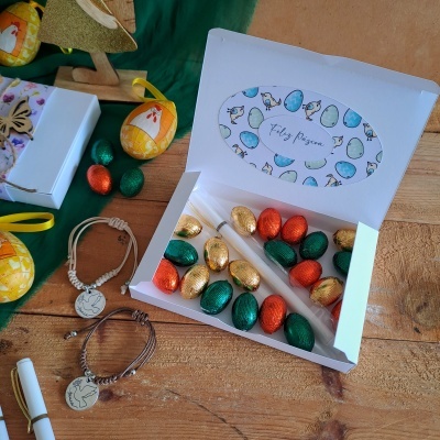 Caixa de chocolates de Páscoa com braceletes e caneta sobre mesa de madeira