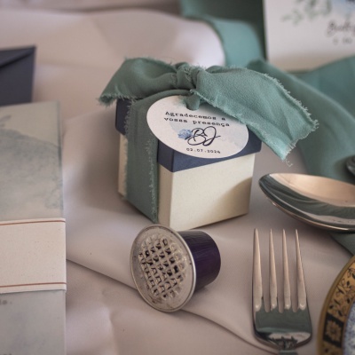 Caixa de presente decorada com faixa verde e etiqueta, sobre mesa com talheres e cápsulas de café