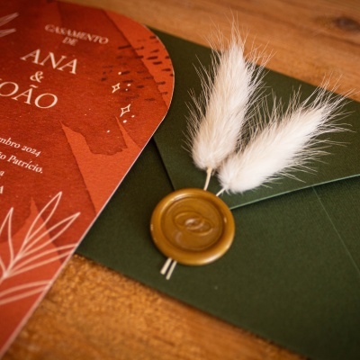 Convite de casamento vermelho e envelope verde com selo e penas brancas