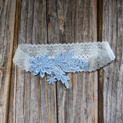 Liga branca de renda com flor azul claro e pérola sobre fundo de madeira