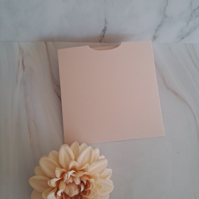 Caixa rosa clara texturizada com flor creme ao lado sobre superfície marmoreada cinza