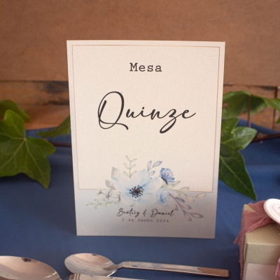 Cartão de mesa branco com texto 'Mesa Quinze' e flores azuis sobre tecido azul