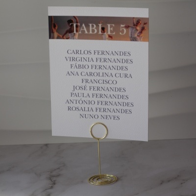 Cartão branco de mesa com texto 'TABLE 5' em fundo colorido e lista de nomes em suporte dourado