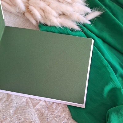 Caderno verde escuro com capa dura sobre tecido cru e verde com raminhos secos