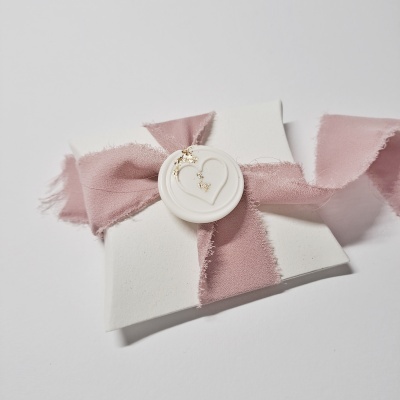 Envelope branco com fita rosa claro e selo branco com coração e brincos dourados