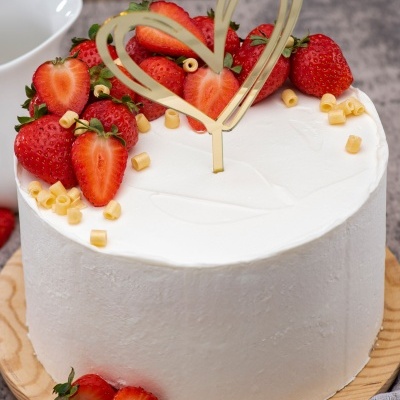 bolo redondo branco com morangos e decoração em forma de coração