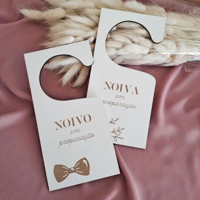 Penduradores de porta casamento em cartão branco com texto em dourado sobre tecido rosa e ramo decorativo