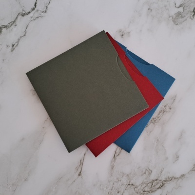 Capas de discos em papel cartão preto, vermelho e azul sobre superfície de mármore