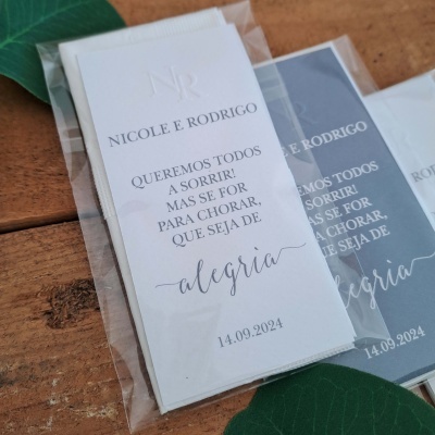 Marcadores de página brancos e cinza com texto em português e data, embalados em plástico sobre madeira e folhas verdes