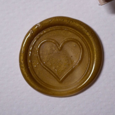 Selo de cera dourado com coração em relevo sobre fundo branco