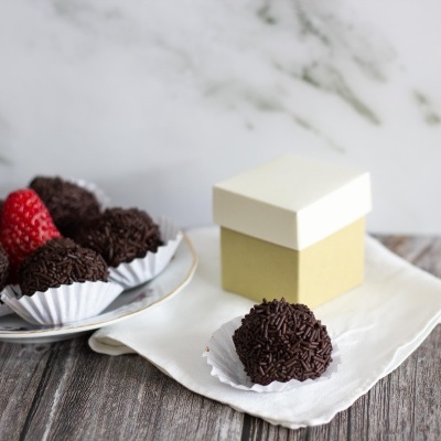 Doces cobertos de chocolate em forminhas brancas com morango e caixa pequena sobre pano branco