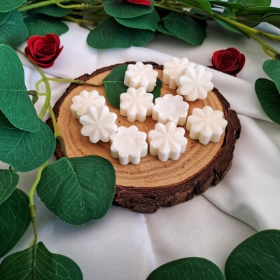 Sabonetes brancos decorativos dispostos em suporte de madeira com folhas verdes e flores vermelhas ao redor