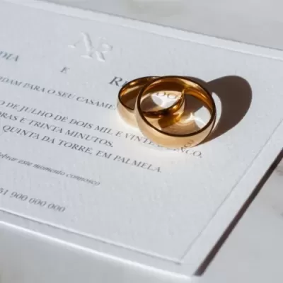 Duas alianças douradas sobre convite de casamento branco com texto em português