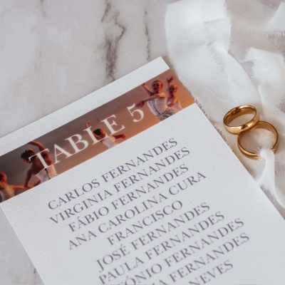 Cartão de mesa com nomes e anéis dourados sobre tecido branco em mesa de mármore.
