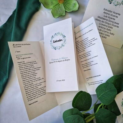 Convites de casamento em papel com texto em português e elementos florais, sobre tecido branco e verde com folhas e flor decorativa.