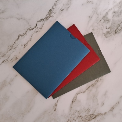 Três capas de pasta de cartão azul, vermelha e cinzenta sobre mármore branco.