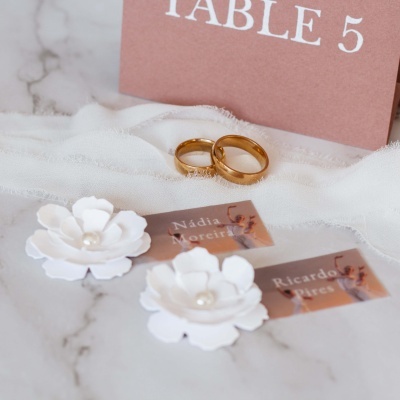 Alianças douradas, cartões de identificação, flores brancas decorativas e cartão 'TABLE 5' sobre superfície de mármore