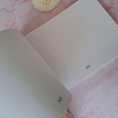 Livro aberto com páginas brancas ao lado de flores sobre mármore rosa