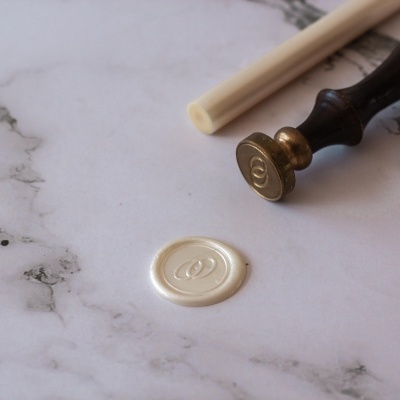 Selo de cera branca com carimbo dourado e cabo preto em superfície marmorizada