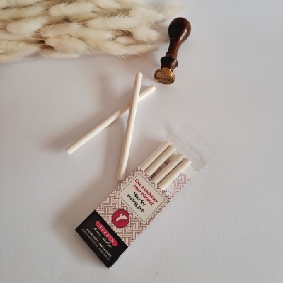 Pacote com palitos de cera branca para selos junto a selo de madeira e penas decorativas