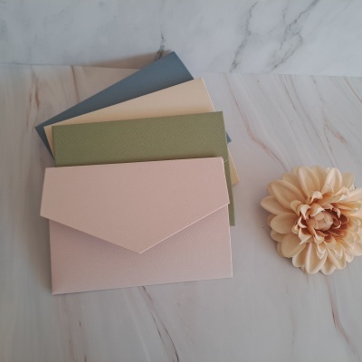 Seis envelopes coloridos com textura dispostos sobre mesa de mármore com flor decorativa ao lado