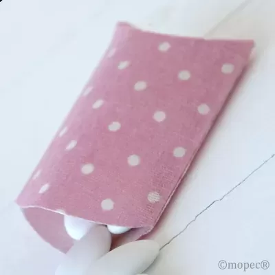 Embalagem rosa com bolinhas brancas e ovais brancos sobre superfície clara.