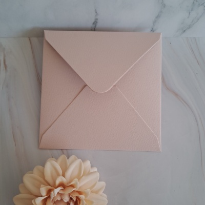 Envelope cor-de-rosa texturizado sobre superfície marmoreada com flor decorativa creme