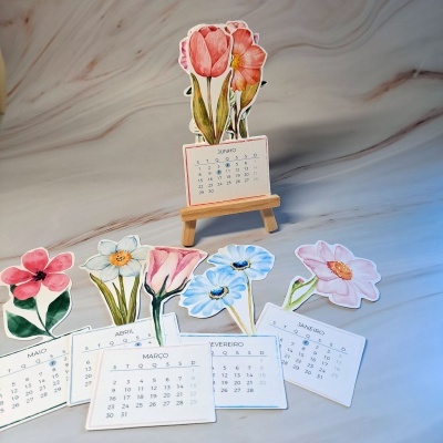 Calendário de mesa floral em cartão com suporte de madeira sobre superfície clara.