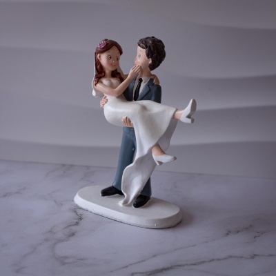 Figurina de noivos a representar casal, noivo a segurar a noiva, cores branco, cinzento, rosa e preto