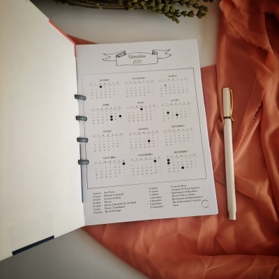 Calendário anual 2023 em página aberta com caneta branca ao lado e tecido cor de pêssego