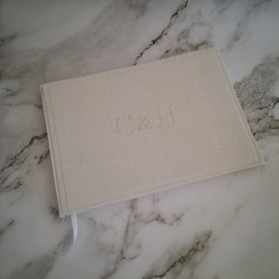 Caderno bege com iniciais C&H em relevo sobre mármore branco