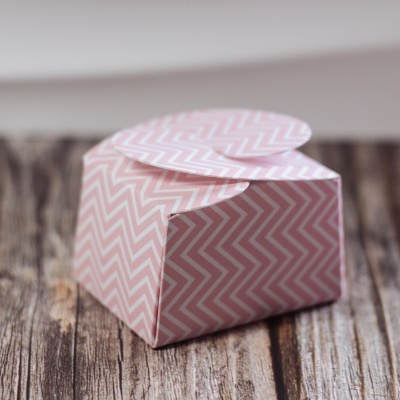 Caixa de papel com padrão ziguezague rosa e branco fechada sobre madeira