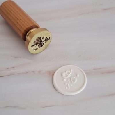 Selo de cera branco com padrão floral e carimbo com pega de madeira.