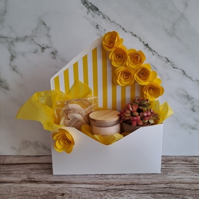 Cesto branco decorado com flores amarelas, planta suculenta, frasco, sabonetes e tecido amarelo.