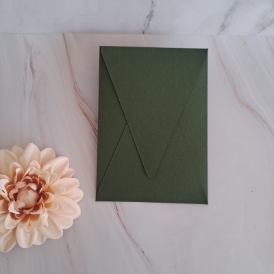 Envelope verde escuro numa superfície branca marmoreada com flor artificial creme