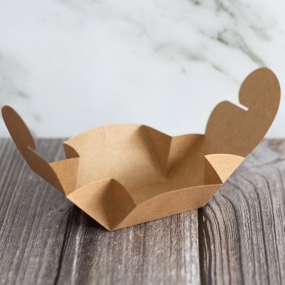 Recipiente de papel castanho claro dobrável com abas em forma de coração numa superfície de madeira.