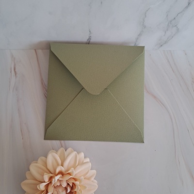 Envelope verde texturizado sobre superfície mármore com flor pêssego