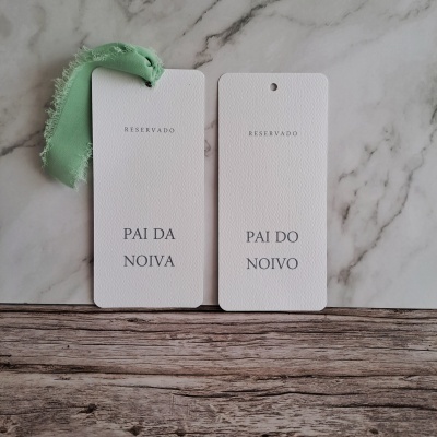 Dois cartões reservados branco com texto preto e fita verde sobre mesa de madeira e fundo mármore