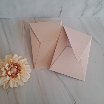 Dois envelopes cor-de-rosa com textura sobre superfície marmoreada ao lado de flor cor-de-rosa