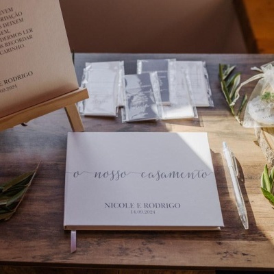 Livro de assinaturas de casamento branco sobre mesa de madeira com caneta, saquinhos e folhas verdes