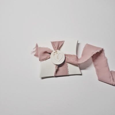 Envelope branco com selo de cera e fita de tecido rosa