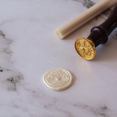 Selo de cera branco com desenho de árvore e carimbo de madeira com parte dourada sobre superfície branca tipo mármore