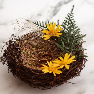 Ninho decorativo com flores amarelas, folhas verdes e raminho seco sobre superfície de mármore