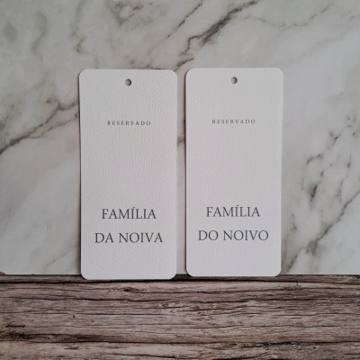 Dois marcadores de papel brancos com texto Reservado Família da Noiva e Família do Noivo sobre superfície de mármore e madeira