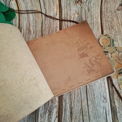 Caderno aberto com ilustração de navio sobre mesa de madeira