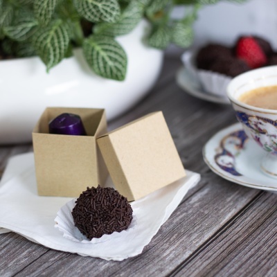 Trufa de chocolate com granulados ao lado de caixa de cartão e chávena decorada