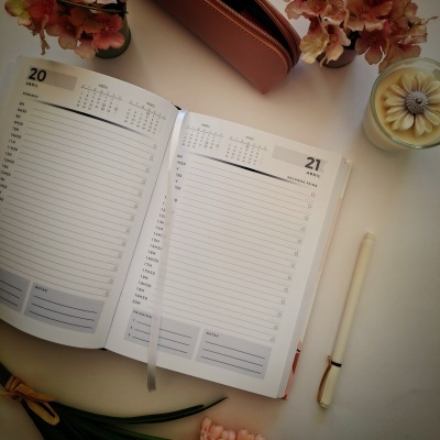 Agenda diária aberta com datas e caneta ao lado sobre mesa branca com vela e flores