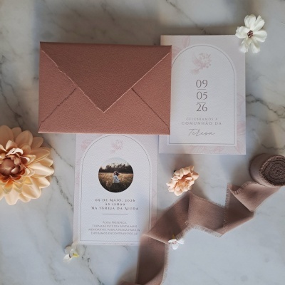 Convite com envelope castanho e flores decorativas sobre mesa de mármore